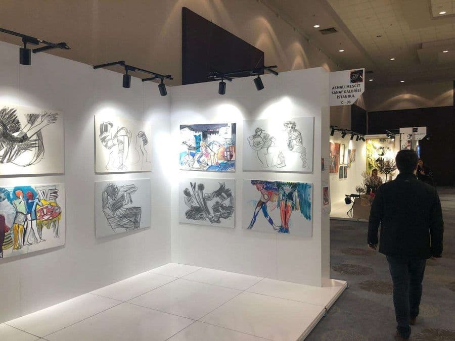 "Asmalı Mescit Sanat Galerisi C-01" isimli standın fuar alanındaki görünümü. Beyaz duvarlarda, figüratif ve dışavurumcu tarzda çizilmiş tablolar sergileniyor.