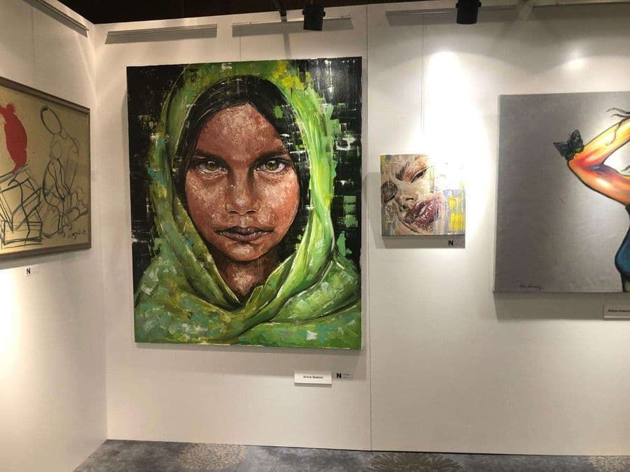 Sanat fuarı alanının yukarıdan görünümü. Odak noktasında duvarlarında asılı olan çeşitli tablolar ve çizimler yer alıyor.