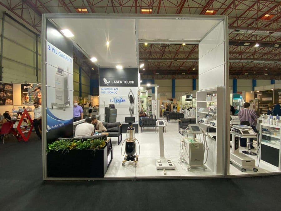 "Laser Touch" markasına ait, estetik ve lazer cihazlarının sergilendiği, kapalı bir ticaret fuarı standı. Standın sağ tarafında "2500W Yeni Nesil IPL" yazılı büyük bir tabela ve bir cihaz sergileniyor. Beyaz raflarda kozmetik ürünler, stant zemininde ise "ICEBERG" yazılı bir cihaz da dahil olmak üzere estetik cihazlar yer alıyor.