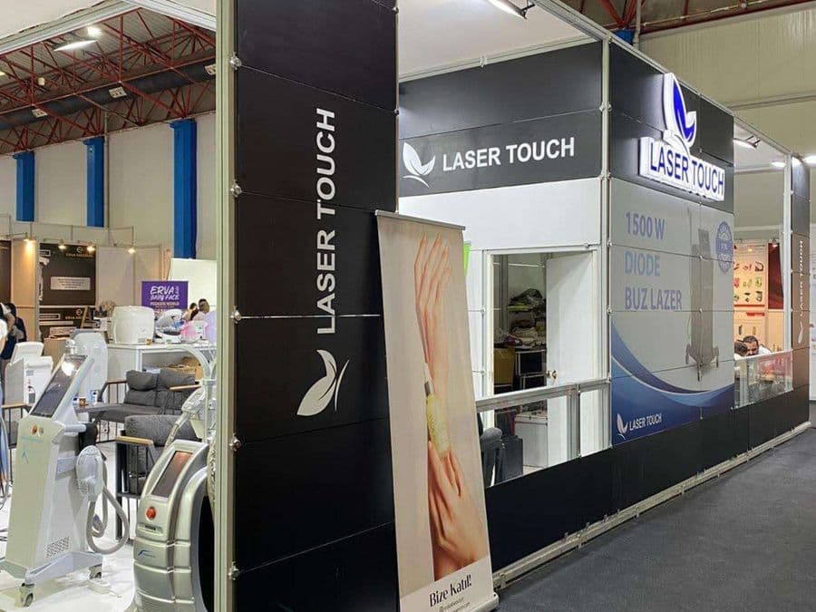 "Laser Touch" markasına ait, estetik ve lazer cihazlarının sergilendiği, kapalı bir ticaret fuarı standı. Standın sağ tarafında "2500W Yeni Nesil IPL" yazılı büyük bir tabela ve bir cihaz sergileniyor. Beyaz raflarda kozmetik ürünler, stant zemininde ise "ICEBERG" yazılı bir cihaz da dahil olmak üzere estetik cihazlar yer alıyor.