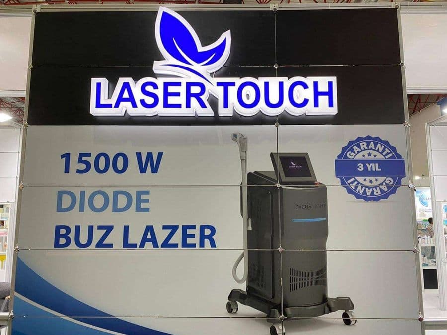 "Laser Touch" markasına ait, estetik ve lazer cihazlarının sergilendiği, kapalı bir ticaret fuarı standı. Standın sağ tarafında "2500W Yeni Nesil IPL" yazılı büyük bir tabela ve bir cihaz sergileniyor. Beyaz raflarda kozmetik ürünler, stant zemininde ise "ICEBERG" yazılı bir cihaz da dahil olmak üzere estetik cihazlar yer alıyor.