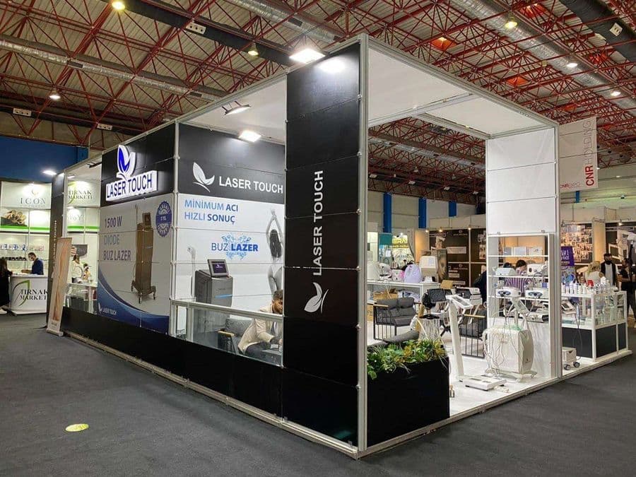 "Laser Touch" markasına ait, estetik ve lazer cihazlarının sergilendiği, kapalı bir ticaret fuarı standı. Standın sağ tarafında "2500W Yeni Nesil IPL" yazılı büyük bir tabela ve bir cihaz sergileniyor. Beyaz raflarda kozmetik ürünler, stant zemininde ise "ICEBERG" yazılı bir cihaz da dahil olmak üzere estetik cihazlar yer alıyor.