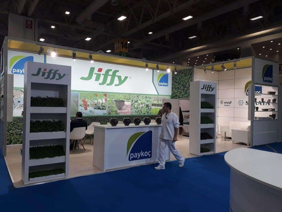 Bahçecilik ürünleri markası "Jiffy"nin bir fuardaki tanıtım standı. Beyaz ve yeşil temalı stantta, bir yanda filizlerin sergilendiği raflar, diğer yanda ise ziyaretçilerin oturduğu masa ve sandalyeler bulunuyor.