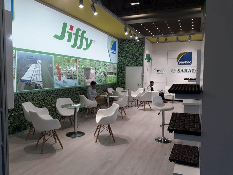 Bahçecilik ürünleri markası "Jiffy"nin bir fuardaki tanıtım standı. Beyaz ve yeşil temalı stantta, bir yanda filizlerin sergilendiği raflar, diğer yanda ise ziyaretçilerin oturduğu masa ve sandalyeler bulunuyor.