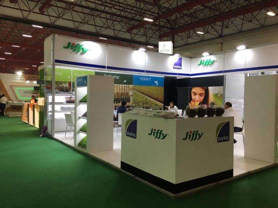 Bahçecilik ürünleri markası "Jiffy"nin bir fuardaki tanıtım standı. Beyaz ve yeşil temalı stantta, bir yanda filizlerin sergilendiği raflar, diğer yanda ise ziyaretçilerin oturduğu masa ve sandalyeler bulunuyor.