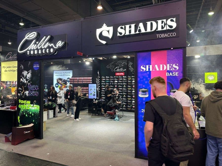 "Chillma Tobacco" ve "Shades Tobacco" markalarının ortak kullandığı büyük ve hareketli bir fuar standı. Ziyaretçilerin yoğun ilgi gösterdiği standın içinde bir berberin saç kestiği görülürken, diğer yanda insanlar nargile içiyor.
